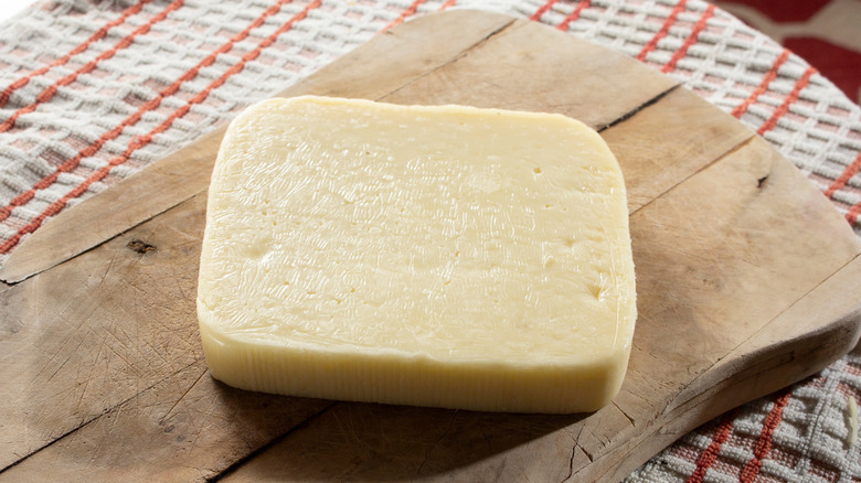 A wedge of brick cheese on a wooden cutting board on top of a kitchen towel