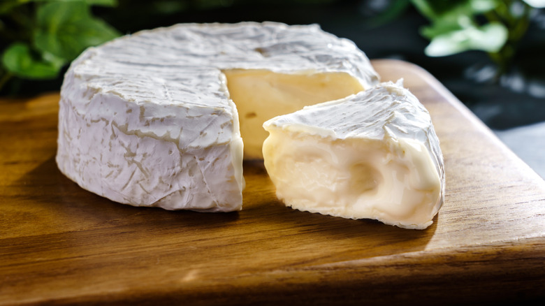 A wheel of Camembert with a wedge cut from it on a wooden board
