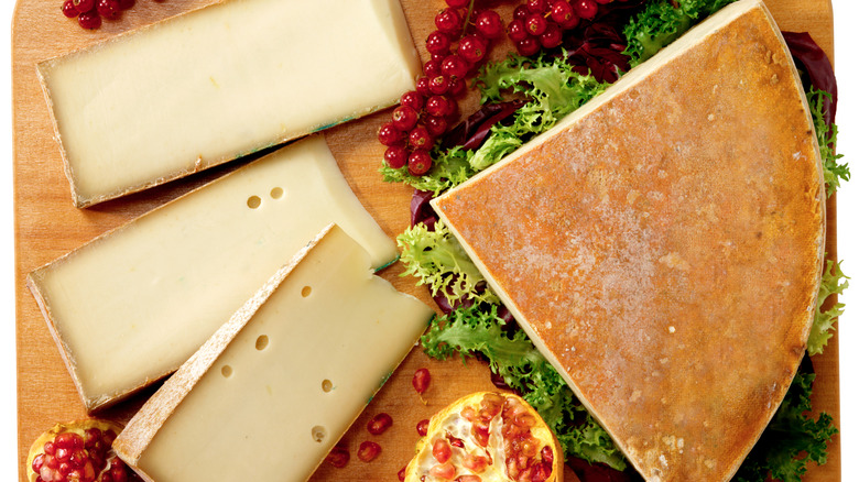 Wedges of Fontina cheese on a platter with assorted fruits and lettuce leaves