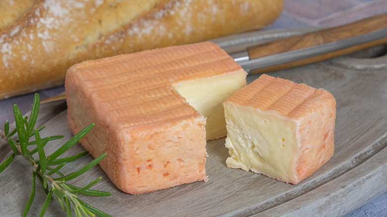 A whole wheel of Maroilles on a board with a baguette