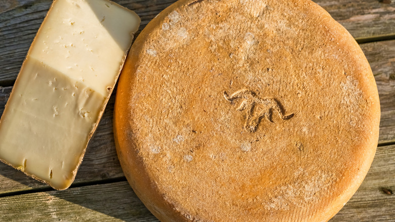 A whole wheel and a wedge of Ossau-Iraty on a wooden table