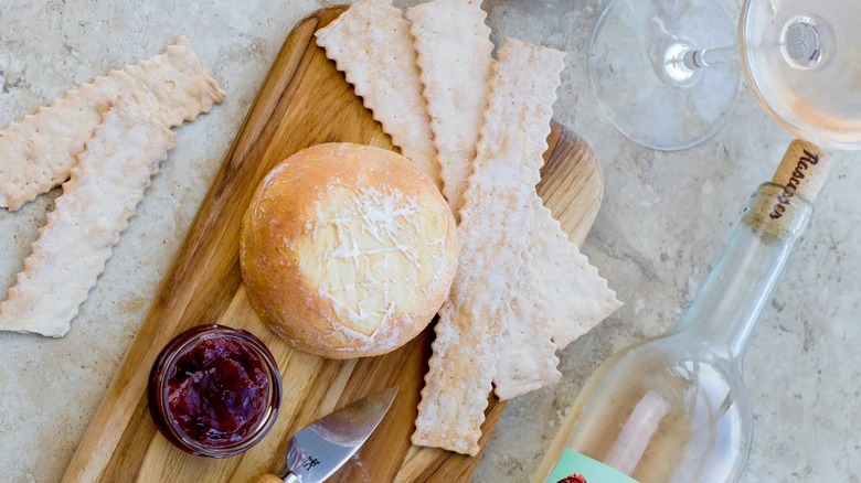 A full wheel of Cowgirl Creamery's Red Hawk on a wooden board with crackers and jams next to wine