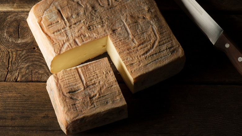 A wheel of Taleggio with one quarter cut on a wooden surface next to a knife