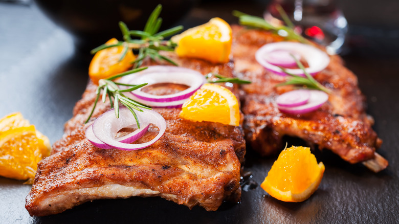 Barbecued pork ribs topped with orange slices, red onion, and herbs