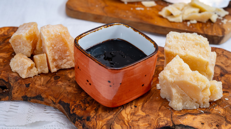 Blocks of Italian parmesan hard cheese from Parmigiano-Reggiano on a wood platter, with balsamico vinegar from Modena in a square orange dish