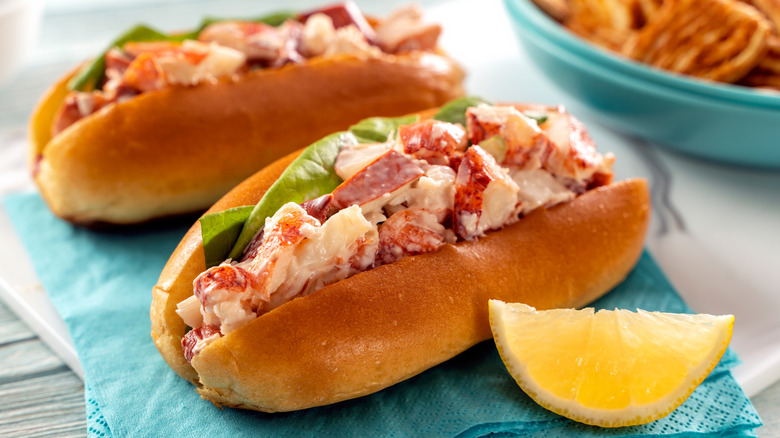 A close-up image of two creamy lobster rolls with leafy greens.