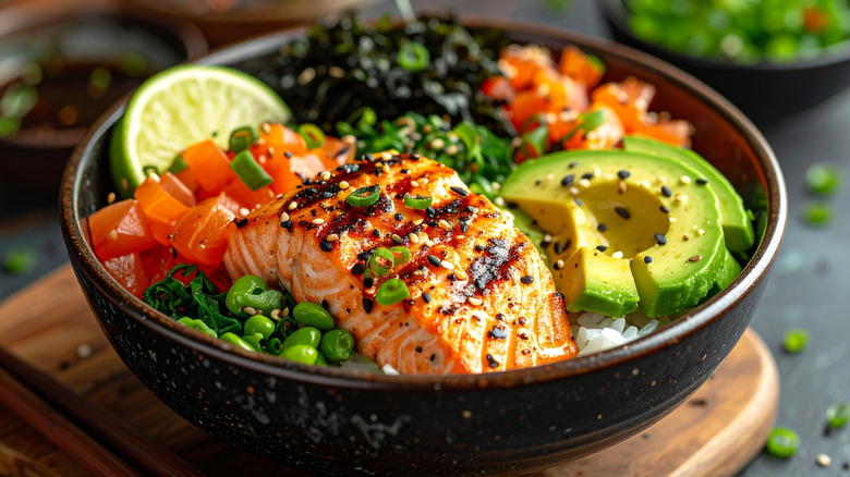 A bowl contains rice, grilled salmon, avocado, seaweed, edamame, lime and green onion.