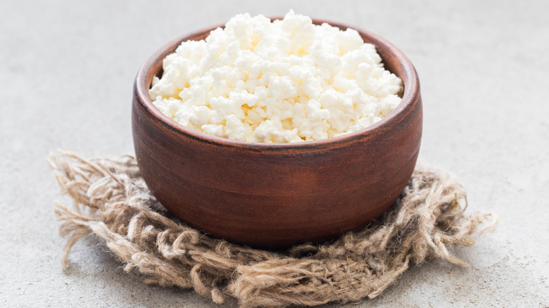 A rustic, clay bowl of cottage cheese on a rustic trivet over a grey countertop.