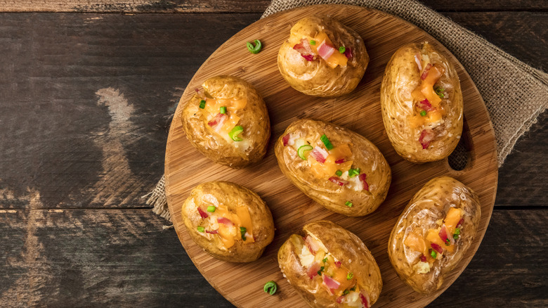 A wooden board with multiple baked potatoes.