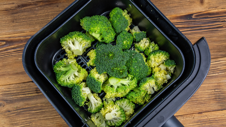 Broccoli in an air fryer basket is photographed from above.