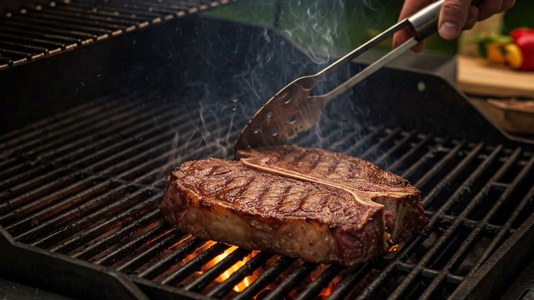 Steaks on a grill being poked with tongs.