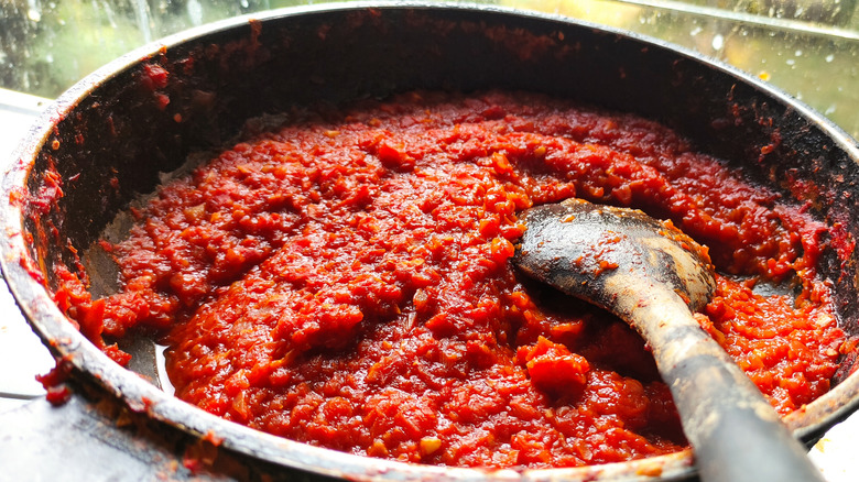 Tomato paste in a pan cooking with a wood spoon settled in it.