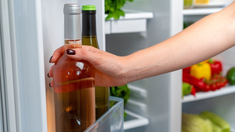 Person reaching for wine bottles in refrigerator door