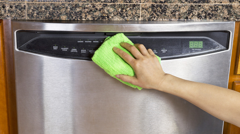 Person cleaning stainless steel dishwasher with a cloth