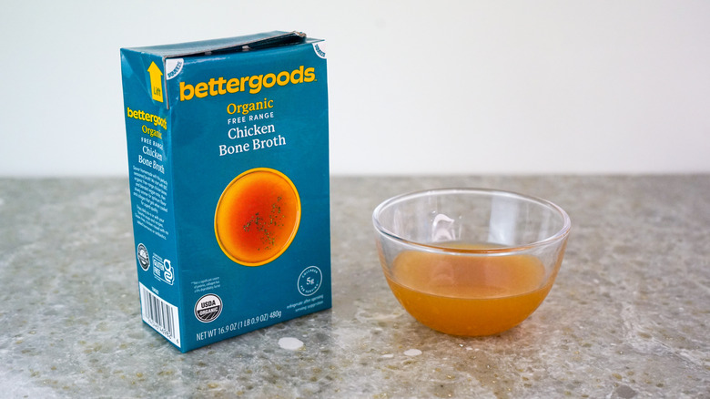 Carton of bettergoods Organic Free Range Chicken Bone Broth next to glass bowl of broth