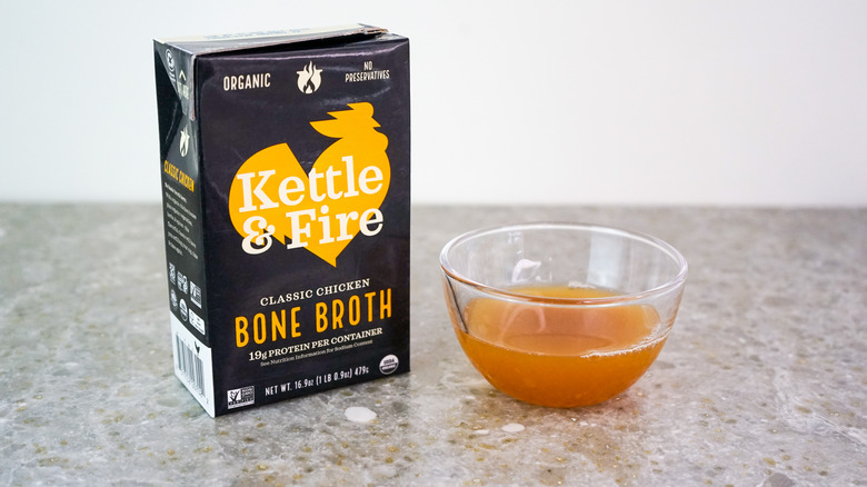 Carton of Kettle & Fire Classic Chicken Bone Broth next to glass bowl of broth