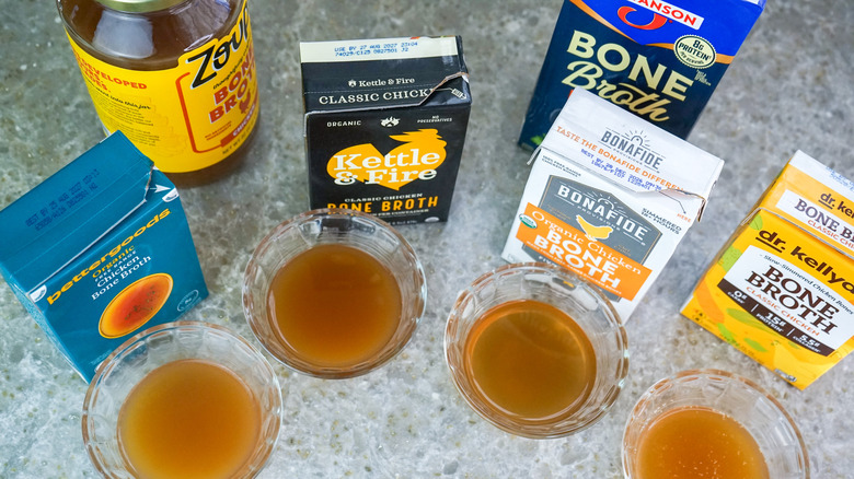 Cartons and jar of chicken bone broth next to glass bowls of broth from above