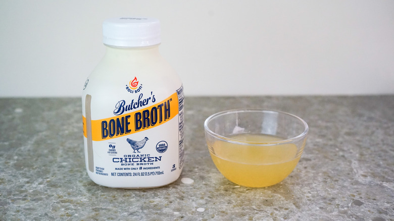 Bottle of Roli Roti Butcher's Bone Broth Organic Chicken Bone Broth next to glass bowl of broth