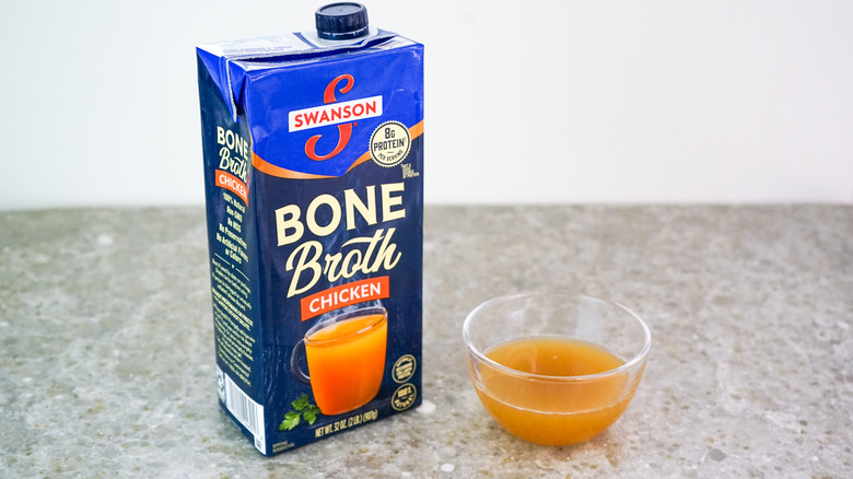Carton of Swanson's Chicken Bone Broth next to glass bowl of broth