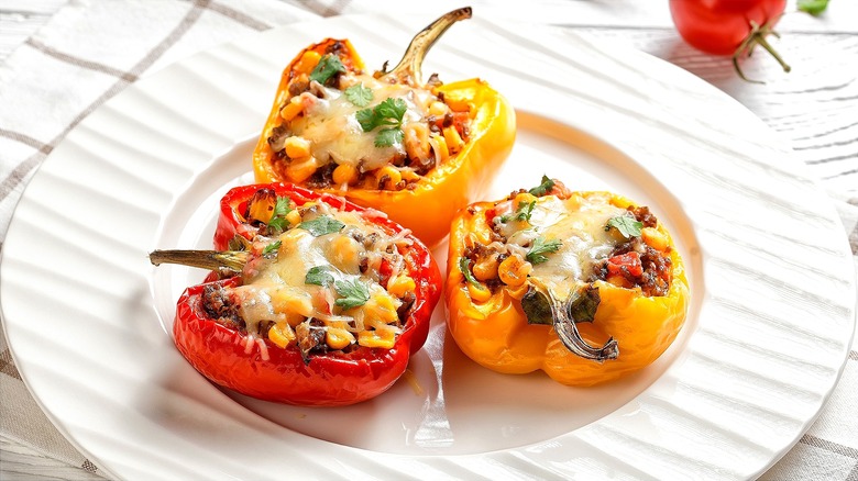 Halved yellow and red bell peppers stuffed with ground meat, corn, and melted cheese on a white plate