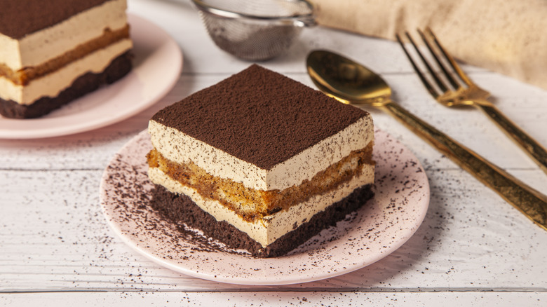Tiramisu on a pink plate with a fork and spoon on the side