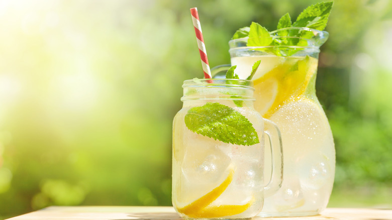 A carafe and a glass of lemonade outdoors.