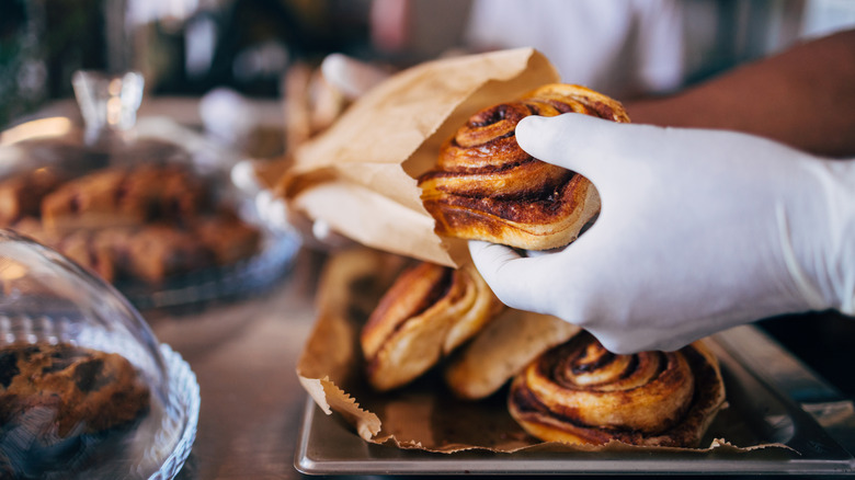 A cinnamon roll being placed in a brown paper bag