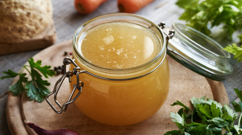 A cozy jar of chicken broth with herbs arranged around it.