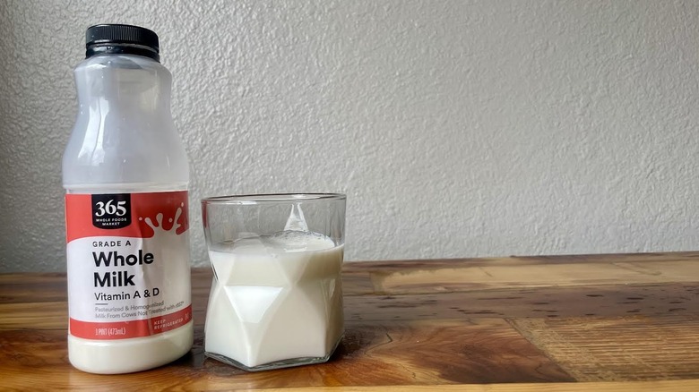 Bottle and glass full of 365 By Whole Foods Market Whole Milk on a wooden table
