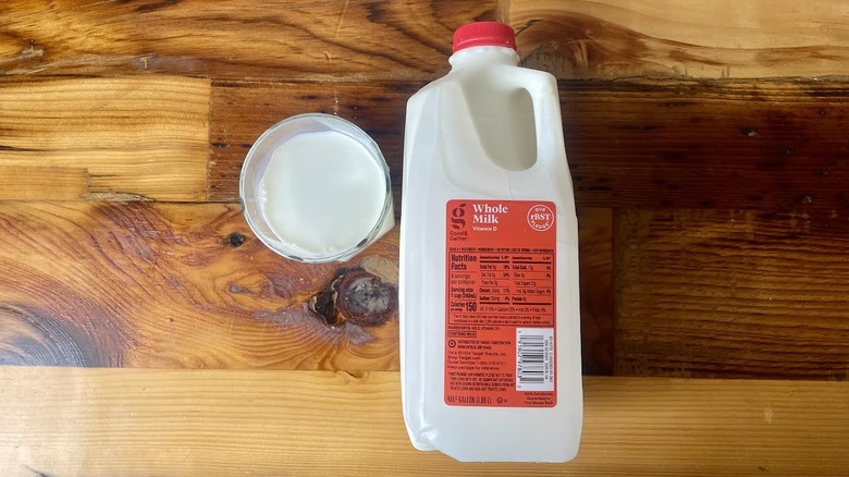Overhead view of a glass and carton of Good & Gather By Target Whole Milk lying on a wooden table top