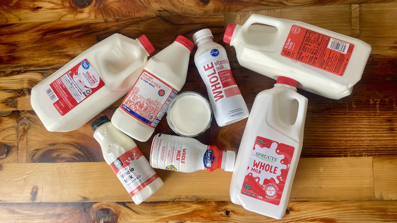 Overhead view of various store-brand milks lying on a wooden table around a glass full of milk