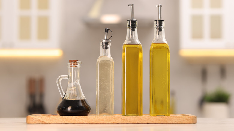 Different glass bottles of salad dressings on a wooden board