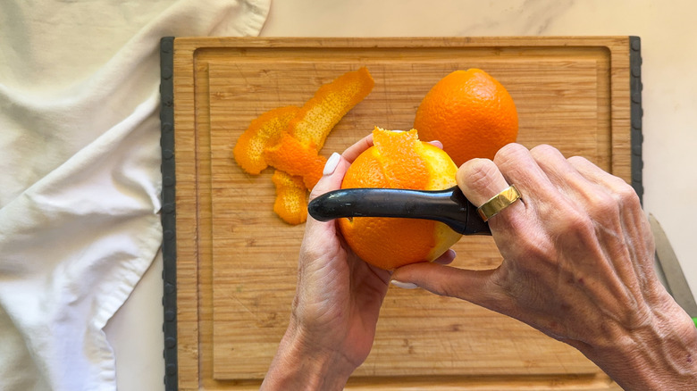 Hands using peeler to peel an orange
