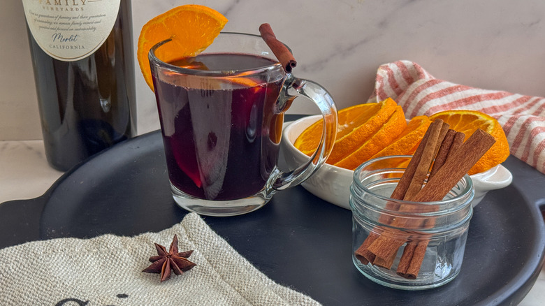mug of mulled wine on tray with orange slices and cinnamon sticks