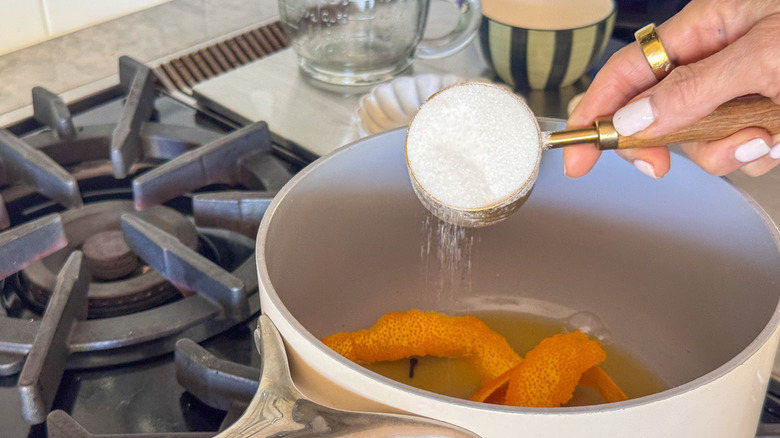 hand adding sugar to pan with orange peels
