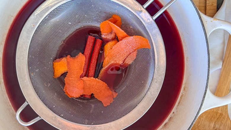 strainer with orange peel and spices over mulled wine