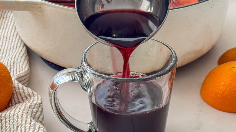 Ladle pouring red mulled wine into clear mug