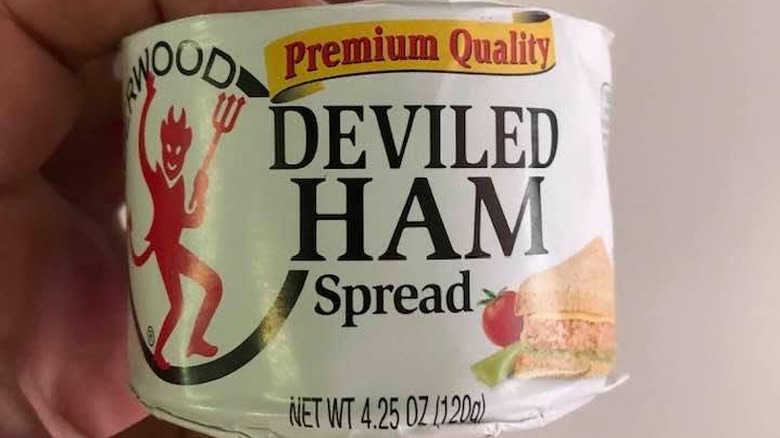 Person's hand holding a paper-wrapped can of Underwood deviled ham spread