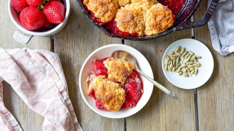 Strawberry and cardamom biscuit cobbler in bowl and serving dish with cardamom pods