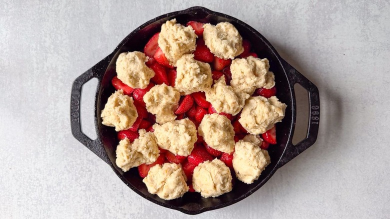 Biscuit dough mounds on top of strawberry cobbler filling in cast iron skillet