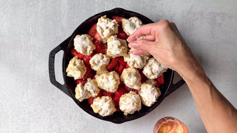 Sprinkling orange sugar on strawberry and cardamom cobbler biscuit dough in cast iron skillet