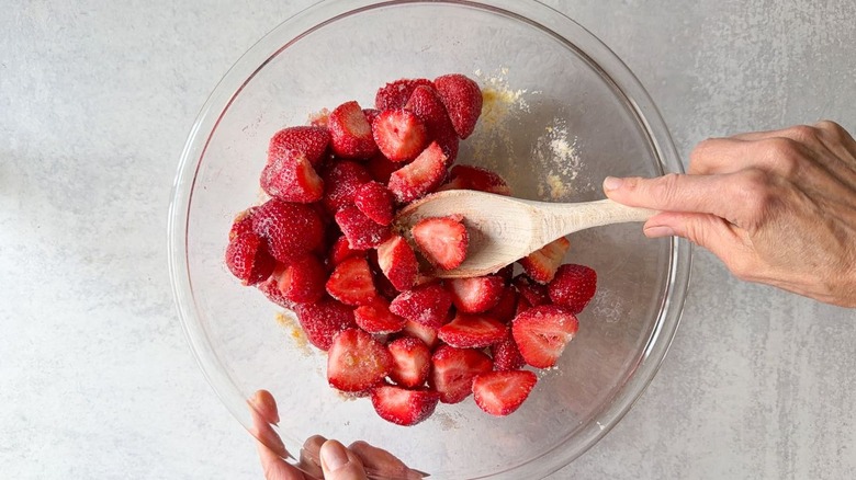 Mixing fresh strawberry halves with orange sugar in glass bowl