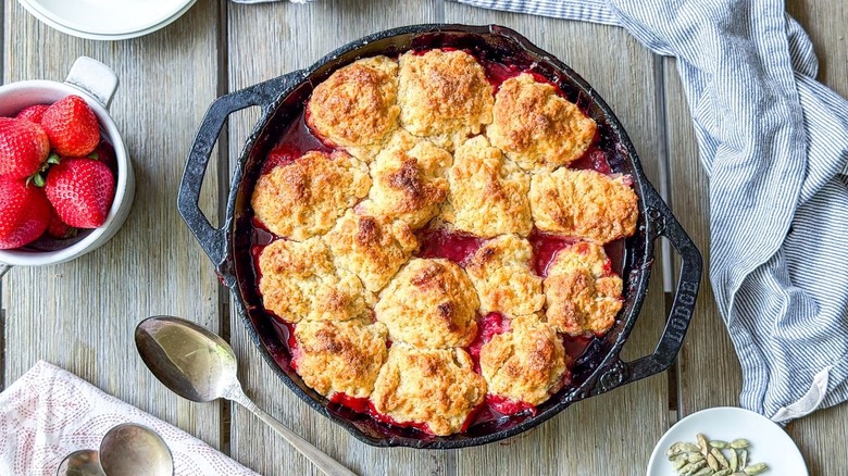Strawberry and cardamom biscuit cobbler in cast iron skillet with fresh strawberries and cardamom pods