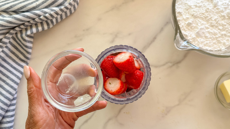 hand adding lemon juice to blender with strawberries