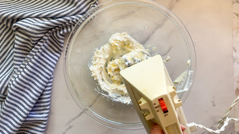 Electric beater mixing butter and cream cheese in bowl