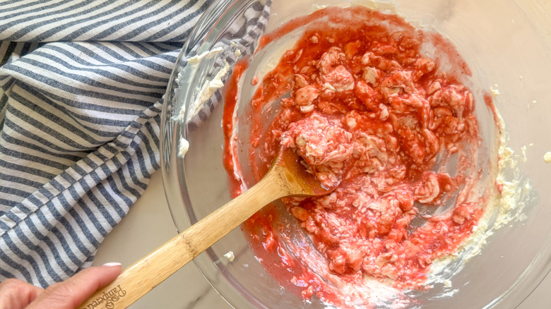 Wooden spoon mixing strawberry puree into cream cheese frosting