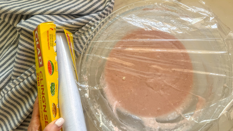 Covering bowl of strawberry frosting with plastic