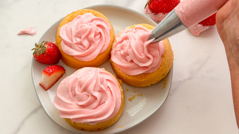 hand piping strawberry frosting onto cupcake
