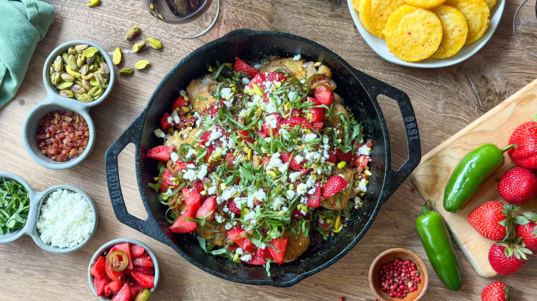 Strawberry jalapeño chicken in cast iron skillet on table with garnishes and crispy polenta