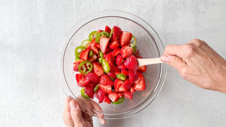 Mixing together pickled strawberries and jalapeños in glass bowl